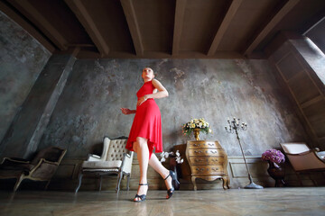 Young woman in red dress dancing tango in retro room, under view