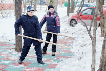 Two boys clean artificial green-red covering of playground with snow shovels