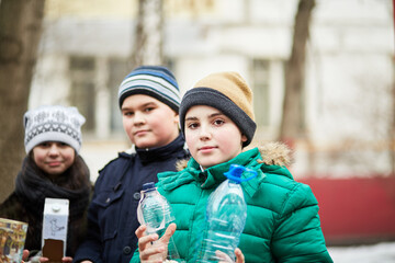 Three children stand together, holding home-made bird feeders with seeds and crumbs
