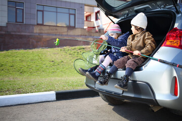 Two children are sitting in open trunk with fishing rod and net