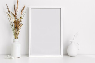 a white frame with a white vase and dried flowers