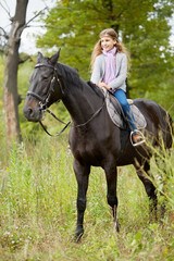 Teenage girl sits on chestnut horse in the park