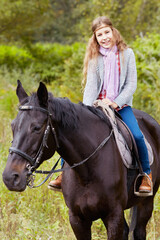 Smiling teenage girl sits on chestnut horse in the park