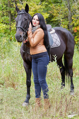 Smiling black-haired woman stands with horse in park.