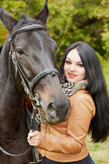 Smiling black-haired woman stands with horse in park.