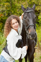 Fototapeta premium Smiling woman with curly hair stands with bay horse in the park