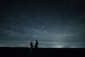The couple holds hands beneath the enchanting night sky, filled with twinkling stars, creating a...