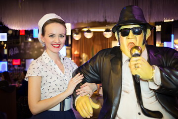 Beautiful young woman in retro dress with waxwork singer in blac