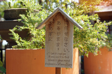 Japanese style wooden sign with messages written in Japanese. English and Thai, which is translated...