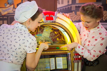 Two girls in retro dress press button on old-fashion musical mac