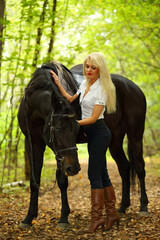 Blonde beautiful woman and black horse in green sunny autumn park