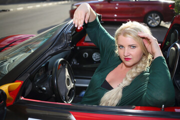 Blonde young woman poses in red sport car at summer sunny day