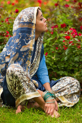 Middle age woman in blue sari and Indian adornment sits on lawn near roses