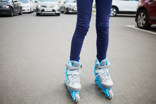 Legs of woman on rollers standing on the carriage way with cars behind.