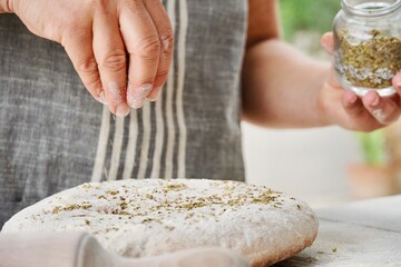 Obraz na płótnie Canvas Bread maker with apron sprinkles spices on top of the bread dough.