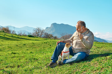 Gray haired man taking a walk with his jack russell dog in meadow in mountainous area. Mature man...