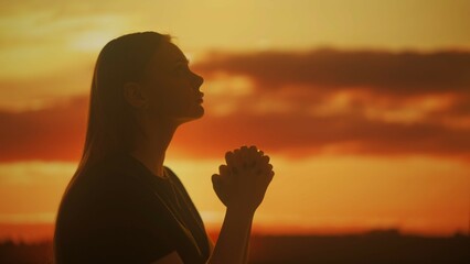 Silhouette of a female praying at sunset