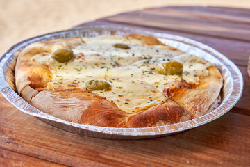 pizza with mozzarella and olives on an aluminum tray on a wooden table, Fast food to enjoy a summer day at the beach or river