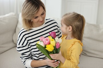 Obraz na płótnie Canvas Little daughter congratulating her mom with bouquet of beautiful tulips at home. Happy Mother's Day