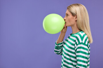 Fototapeta na wymiar Woman blowing up balloon on violet background. Space for text