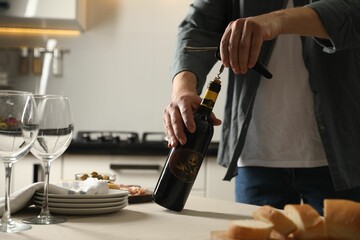 Man opening wine bottle with corkscrew at table indoors, closeup