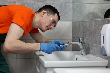 Smiling plumber repairing faucet with spanner in bathroom