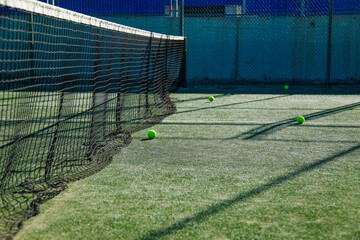 Sunlit tennis court with green balls and net.