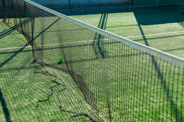 Tennis ball on net, green court.