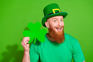 Portrait of excited cheerful person toothy smile arm hold paper clover leaf isolated on green color...