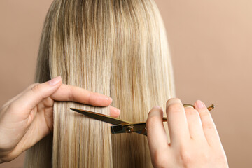 Hairdresser cutting client's hair with scissors on beige background, closeup