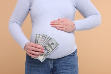 Surrogate mother. Pregnant woman with dollar banknotes on beige background, closeup