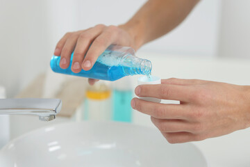 Obraz na płótnie Canvas Young man using mouthwash in bathroom, closeup