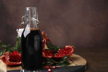 Tasty pomegranate sauce in bottle, fruits and branches on wooden table, closeup. Space for text