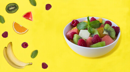 Fruit salad in the white bowl on the yellow background. Copy space. Close-up.
