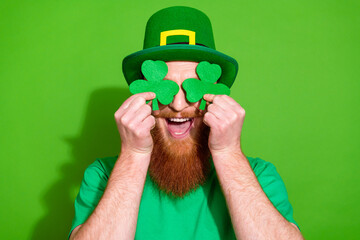Photo of positive man have good mood hold paper clover leaves cover eyes isolated on green color...