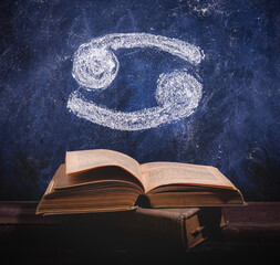 Zodiac sign Cancer on chalkboard above old astrology books.