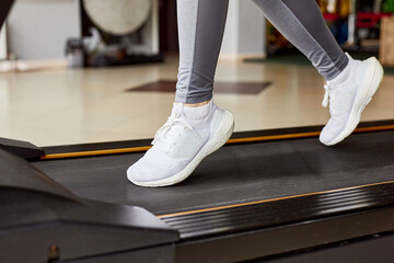 Close-up of a woman's legs in white sneakers on a treadmill. Morning cardio workout. Running in the...