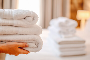 Close-up of Hand professional chambermaid putting stack of fresh towels in hotel room. Hotel room in blur in background.