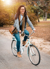 Relaxed, happy young female with wide smile riding a bike during the late afternoon in the city park on her way from work to home.