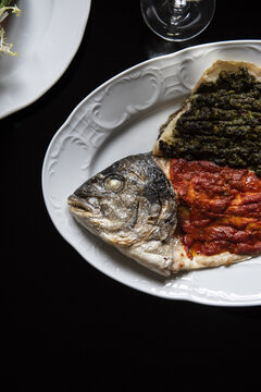 Whole fish on a plate in restaurant with red and green sauces