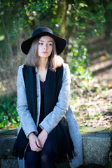 A lonely girl in a black hat sits in on a summer theater bench