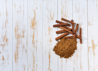 cinnamon sticks and cinnamon powder on a white wooden table, top view.