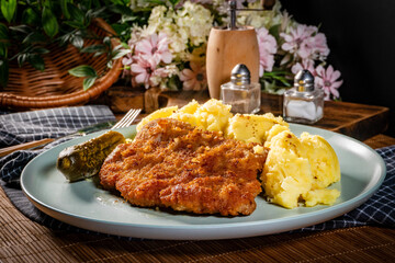 Breaded pork neck cutlet served with potatoes and pickled cucumber.