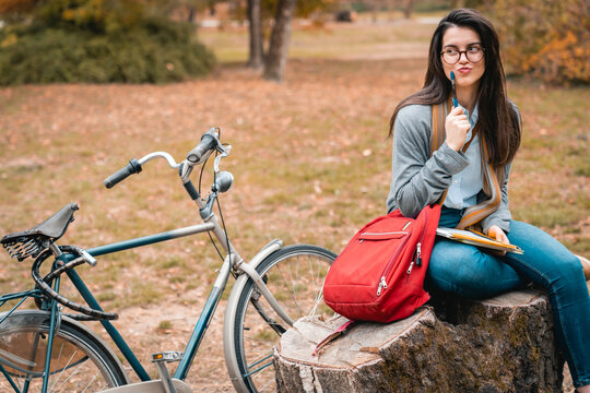 Young college student trying to focus on studying outdoors. Attractive girl sitting in public park thinking of a way to improve her work.