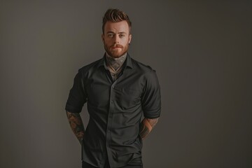 A man with a beard and tattoos stands in front of a gray background