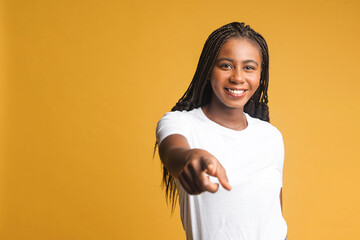 Glad delighted woman with dreadlocks indicating with both fore fingers at you, picks up someone, inviting to join her, has happy friendly expression. Indoor studio shot isolated on yellow background