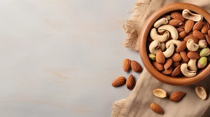 Fotobehang Almonds, pistachios, and cashews arranged in a wooden bowl on a linen napkin, set against a light grey background. (Horizontal view with space for text) © Shabnam