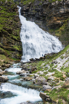 A hiker stands by a roaring waterfall in the Ordesa Valley, showcasing the scale and beauty of the Parque Nacional de Ordesa y Monte Perdido