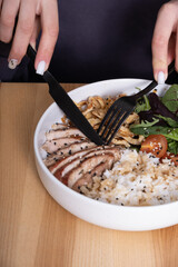 Hands with utensils over a bowl of meat, rice and vegetables.