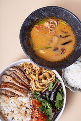 Bowl with rice, veal and vegetables and tom yam soup angle view.